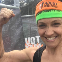 Smiling woman wearing Tough Mudder headband and flexing her arm muscles