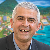 Smiling man with short grey hair in front of colourful landscape painting
