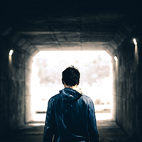 Back of a man in a hoodie in a tunnel looking towards the light