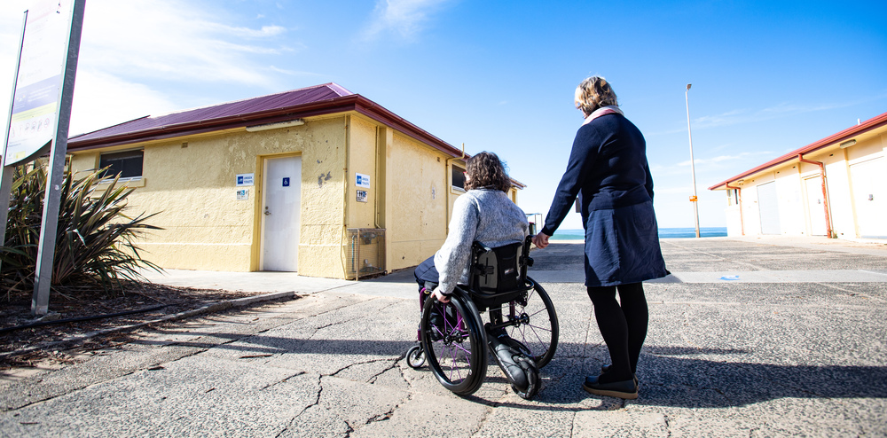 Woman in wheelchair with friend near accessible toilet at Thirroul Beach Pavilion