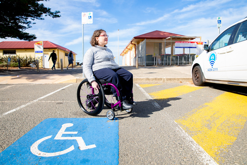 Woman in wheelchair at Thirroul Beach accessible parking space, with concourse in background